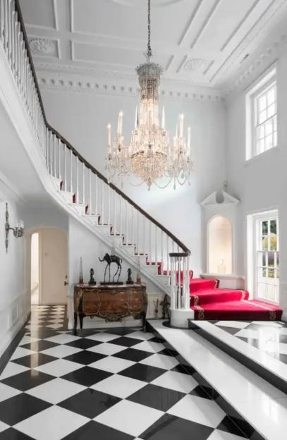 Grand foyer with a large chandelier, staircase with red runner, and black and white checkered floor.