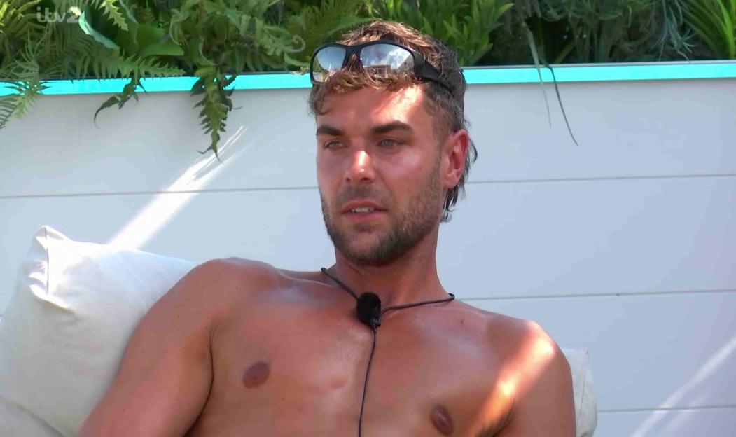 Man sitting shirtless, wearing sunglasses.