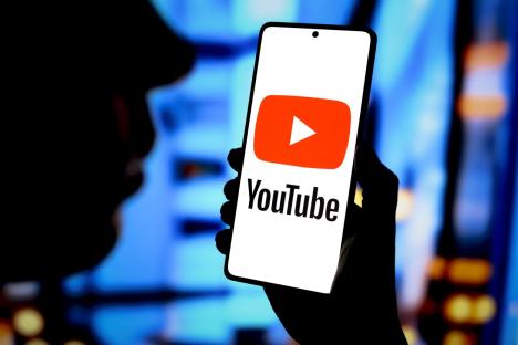 Photo illustration of a hand holding a smartphone displaying the YouTube logo.