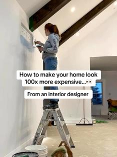 Woman on ladder painting wall to make home look more expensive.
