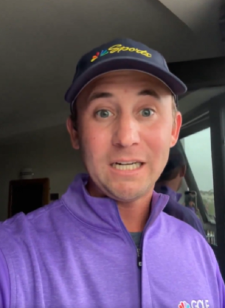 Man in purple shirt and baseball cap looking at camera.
