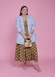 Woman in a polka dot dress and lavender blazer holding a handbag.