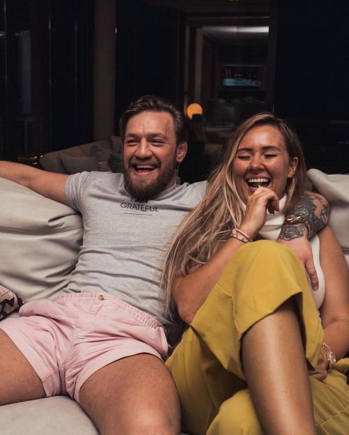 Dee Devlin and Conor McGregor laughing together on a couch.