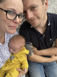 A family selfie: parents holding their newborn baby.