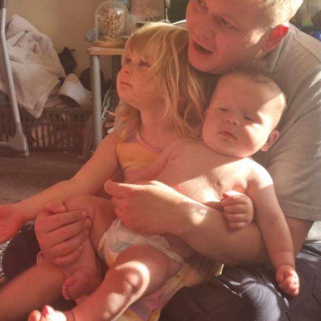 A large baby sitting with a toddler and adult.