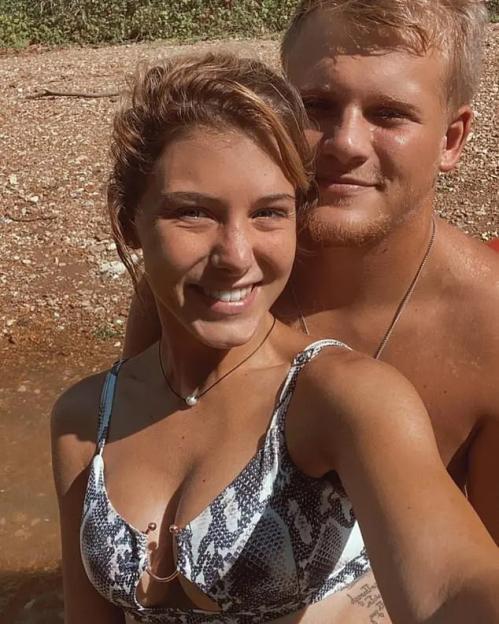 A young woman and man posing for a selfie. The woman is wearing a snakeskin-print bikini top.