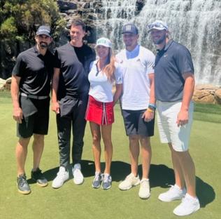 Group photo of five people on a golf course in front of a waterfall.