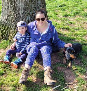 A mother and her young son sit with their dog near a tree.