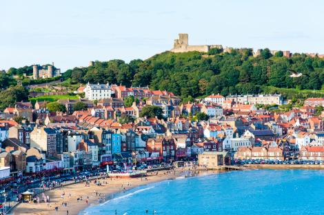 View of Scarborough South Bay harbor, England, with a castle on a hill overlooking the town and beach.