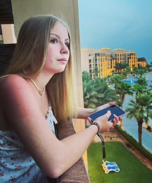 Teenage girl looking out from a balcony, holding a phone.