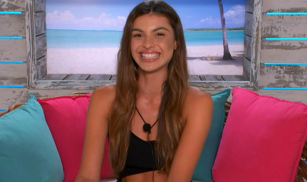 Smiling woman sitting on a couch in front of a beach scene.