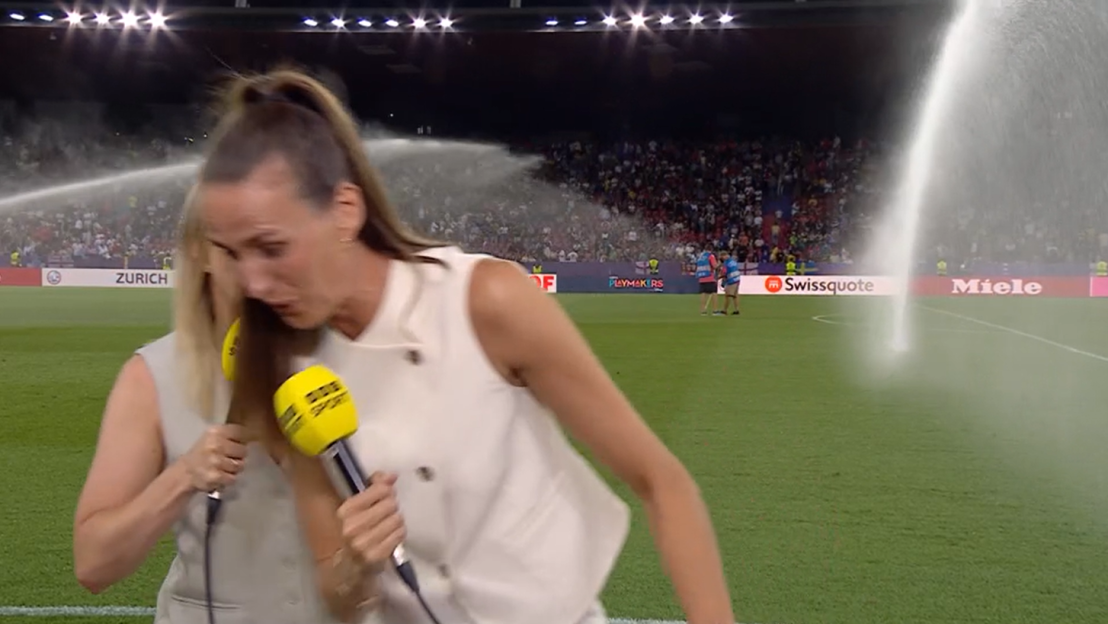 Reporter being sprayed by sprinklers during a soccer game interview.