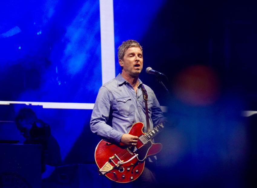 Noel Gallagher playing guitar on stage.
