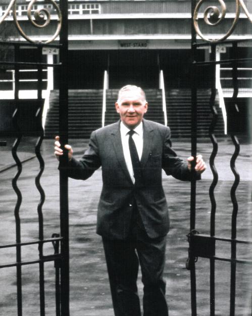 Man in suit standing at gate to West Stand.