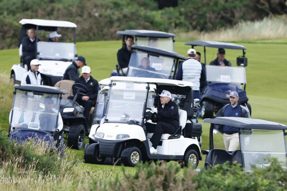 Donald Trump in a golf cart on a golf course.