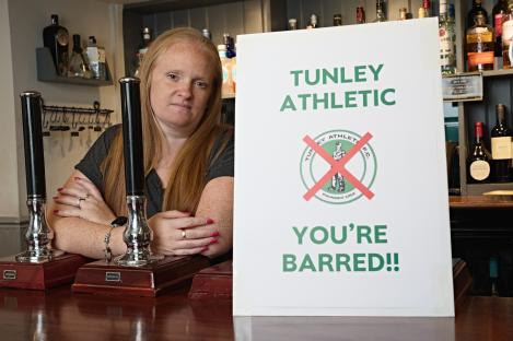 A pub landlady with a sign banning Tunley Athletic.