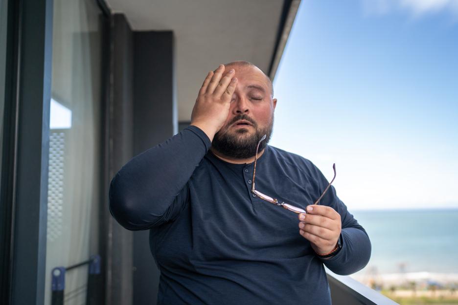Overweight man on balcony with headache.