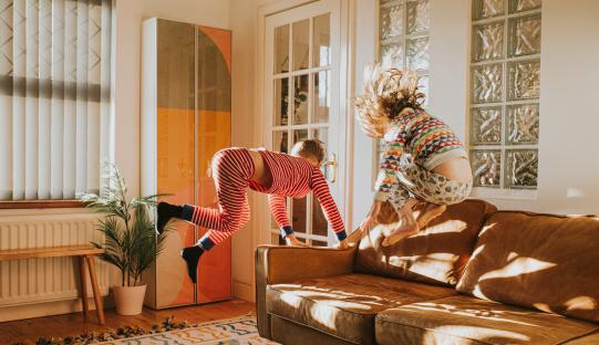 Two children in pajamas jumping on a couch.