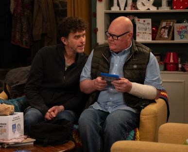 Two men sitting on a couch, one holding a video game.