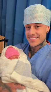 A man in scrubs holding a newborn baby wrapped in a towel.