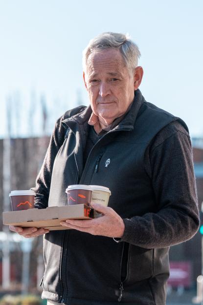 Ian Wilkinson holding two takeaway coffees outside a courthouse.