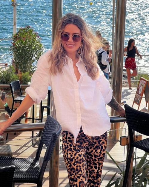 Woman in white shirt and leopard print pants at an outdoor cafe by the sea.