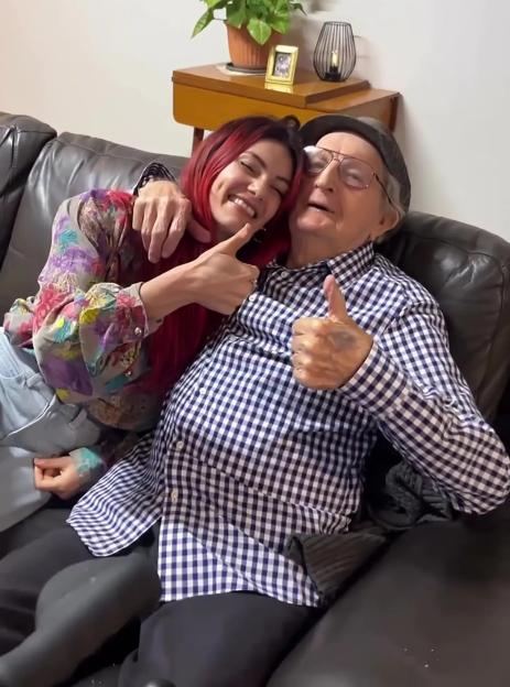 Woman and her grandfather giving thumbs up on a couch.
