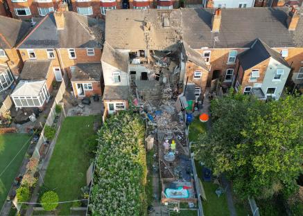 Aerial view of firefighters examining a house damaged by an explosion.