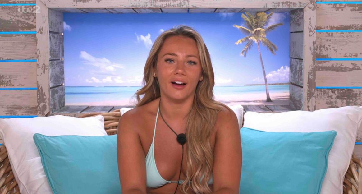 Paige from Love Island sits on a bed.
