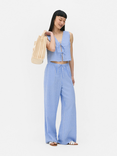 Woman in blue striped pants and matching top holding a straw bag.