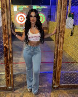 Woman in True Religion top and jeans at an axe throwing venue.