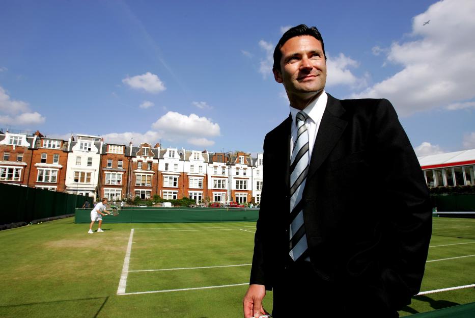 a man in a suit stands in front of a tennis court