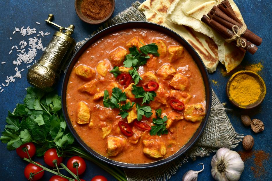Chicken tikka masala in a bowl with naan bread and spices.