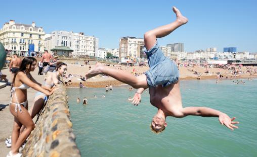 Person backflipping into ocean at crowded beach.