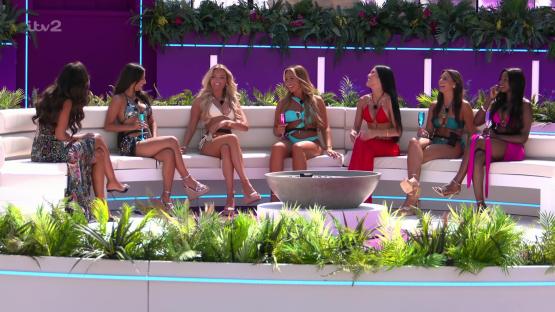 Six women in swimwear sitting on a couch, talking.