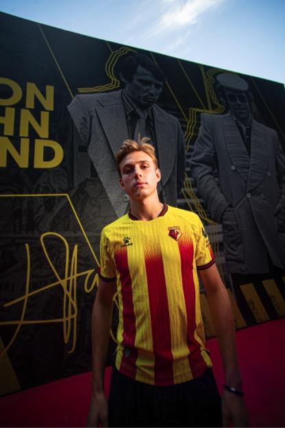 Man in Watford FC jersey standing in front of a mural.