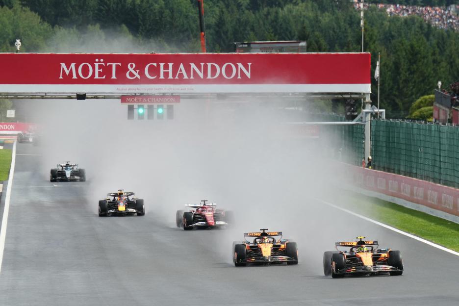 Formula One race cars driving through a spray of water.