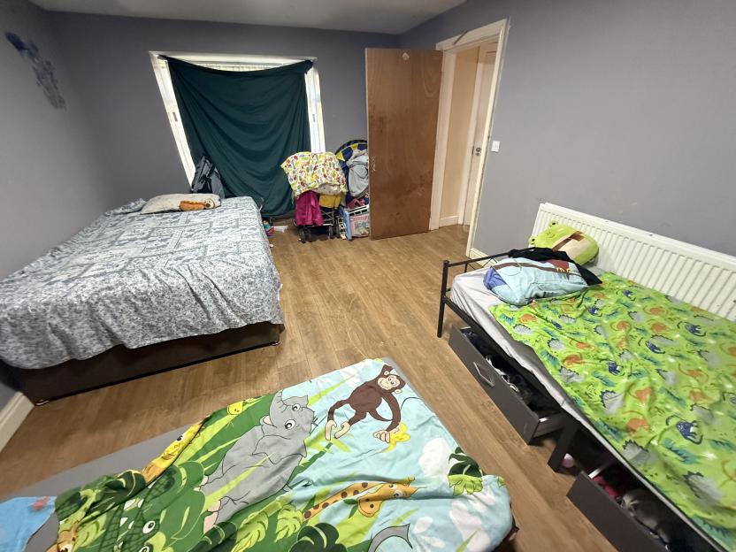 A cluttered bedroom with two beds and a partially covered window.
