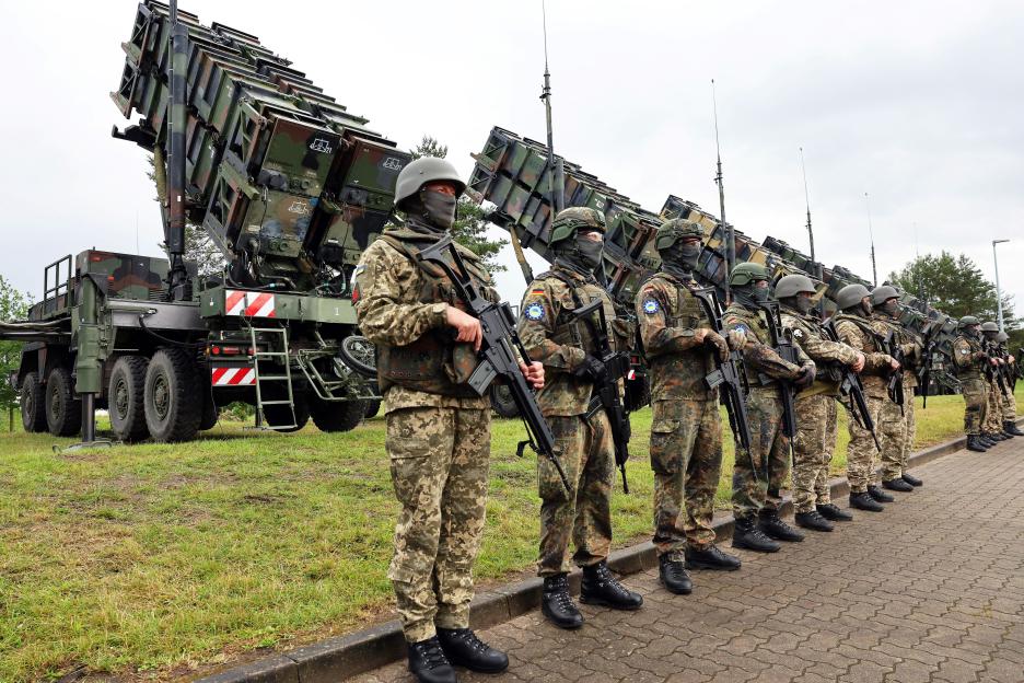 Ukrainian and German soldiers standing in formation with Patriot missile launchers.