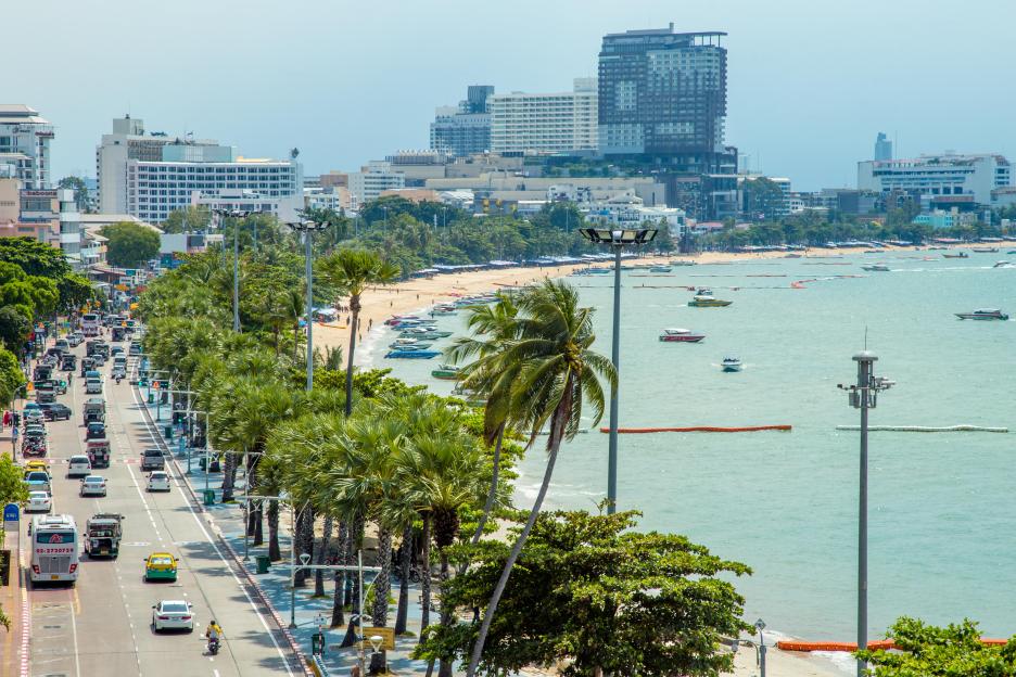 Pattaya Beach road scene with beach, ocean, palm trees, and buildings.