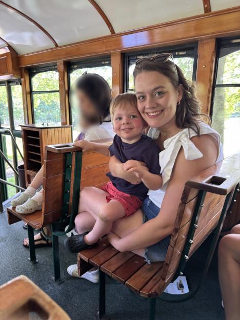 A woman and young child sitting on a wooden bench on a trolley.