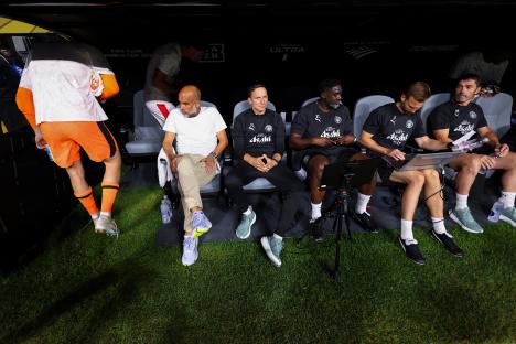 Pep Guardiola and his coaching staff seated on the sidelines.
