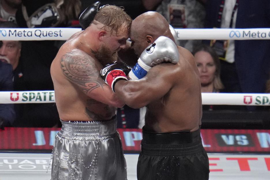 Jake Paul and Mike Tyson embracing in a boxing ring.