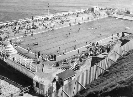 Black and white photo of Tynemouth outdoor swimming pool with many people swimming and sunbathing.