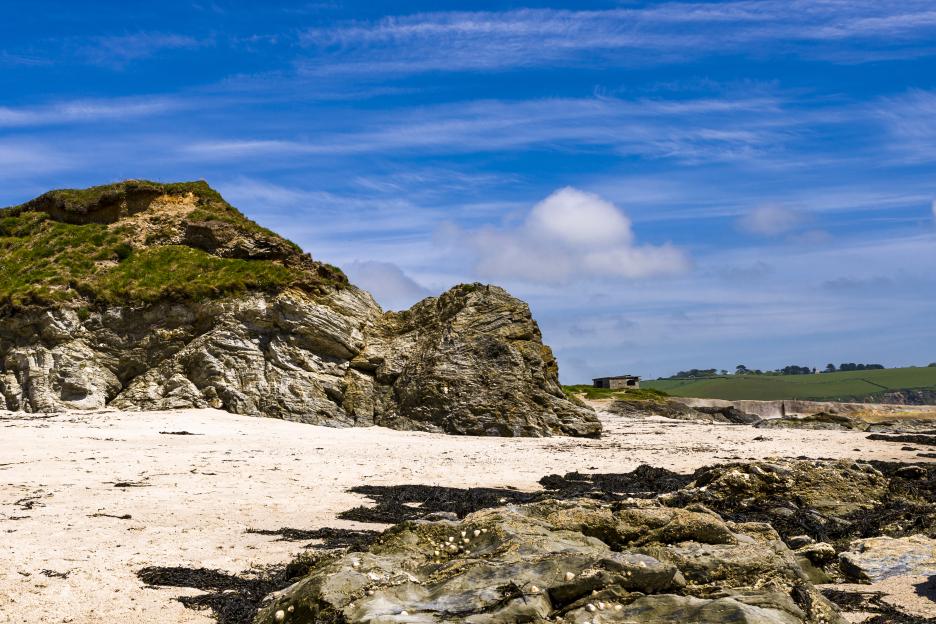 Wide angle view of Par Sands bay, showing rocks, sand, and a small building.
