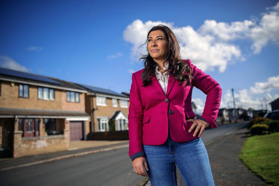 A woman in a pink blazer stands on a residential street.