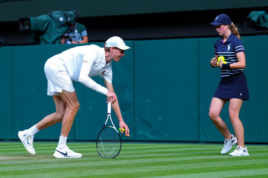 Jannik Sinner handing a champagne cork to a ball girl at Wimbledon.