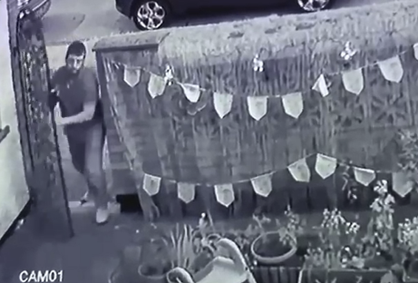Black and white security camera footage of a man entering a gate.