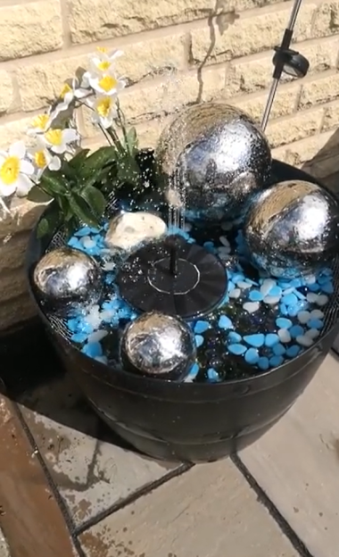 Solar-powered fountain with metallic spheres and flowers.