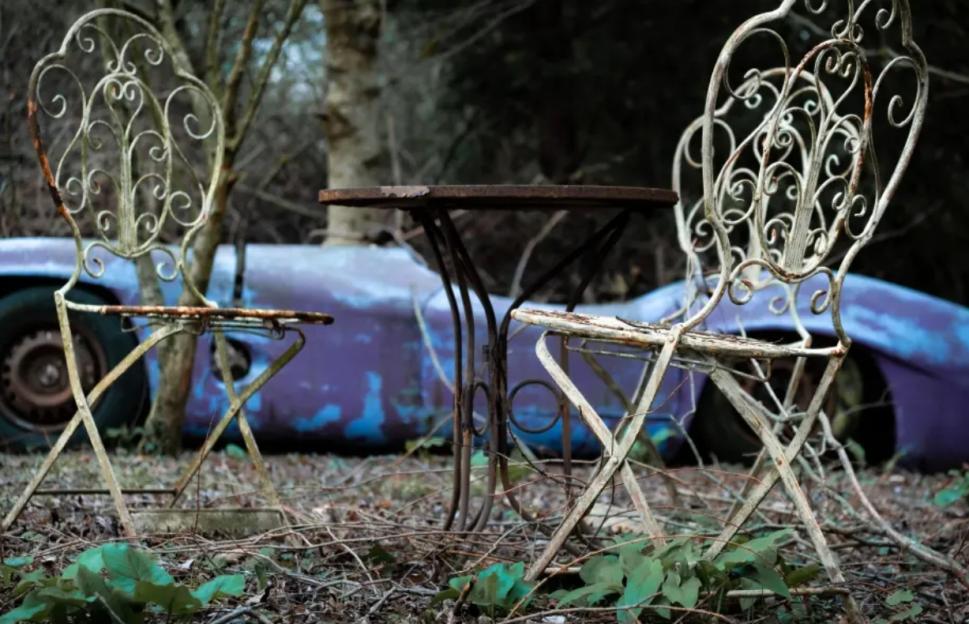 Rustic metal table and chairs in front of a damaged car.